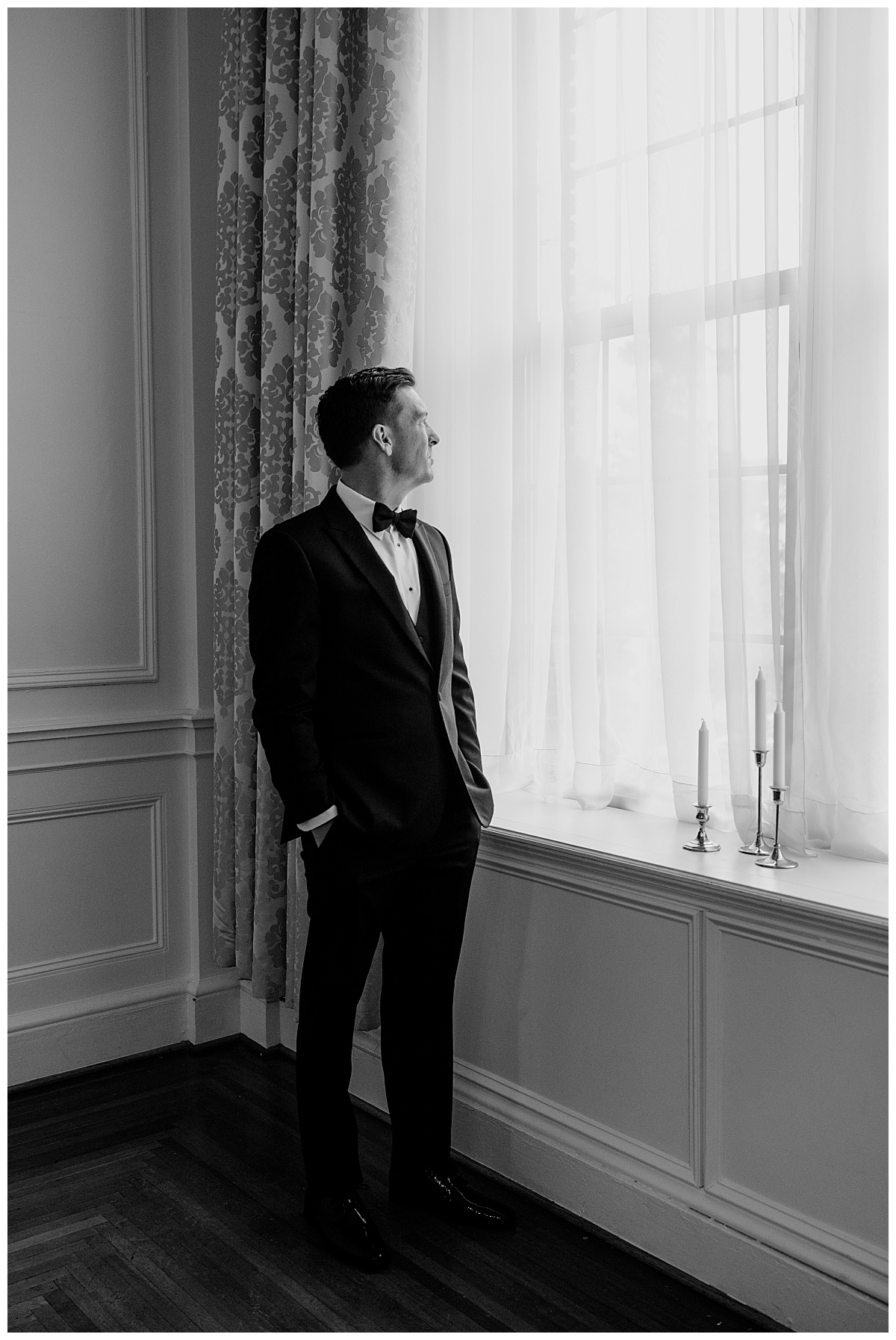man stands by window with hands in pockets by The Hazel Club