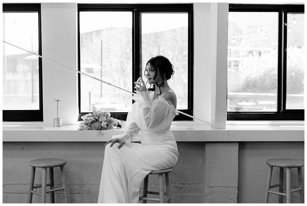 woman sips drink sitting at bar in front of windows by The Hazel Club