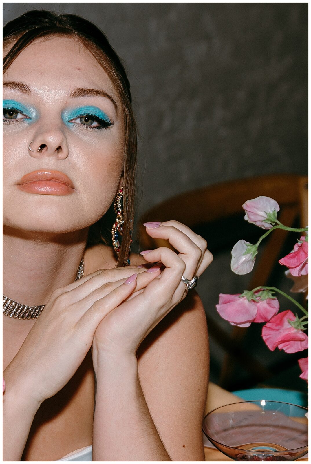 model with bright blue eye shadow and nose ring looks straight ahead while seated by Charlotte wedding photographer
