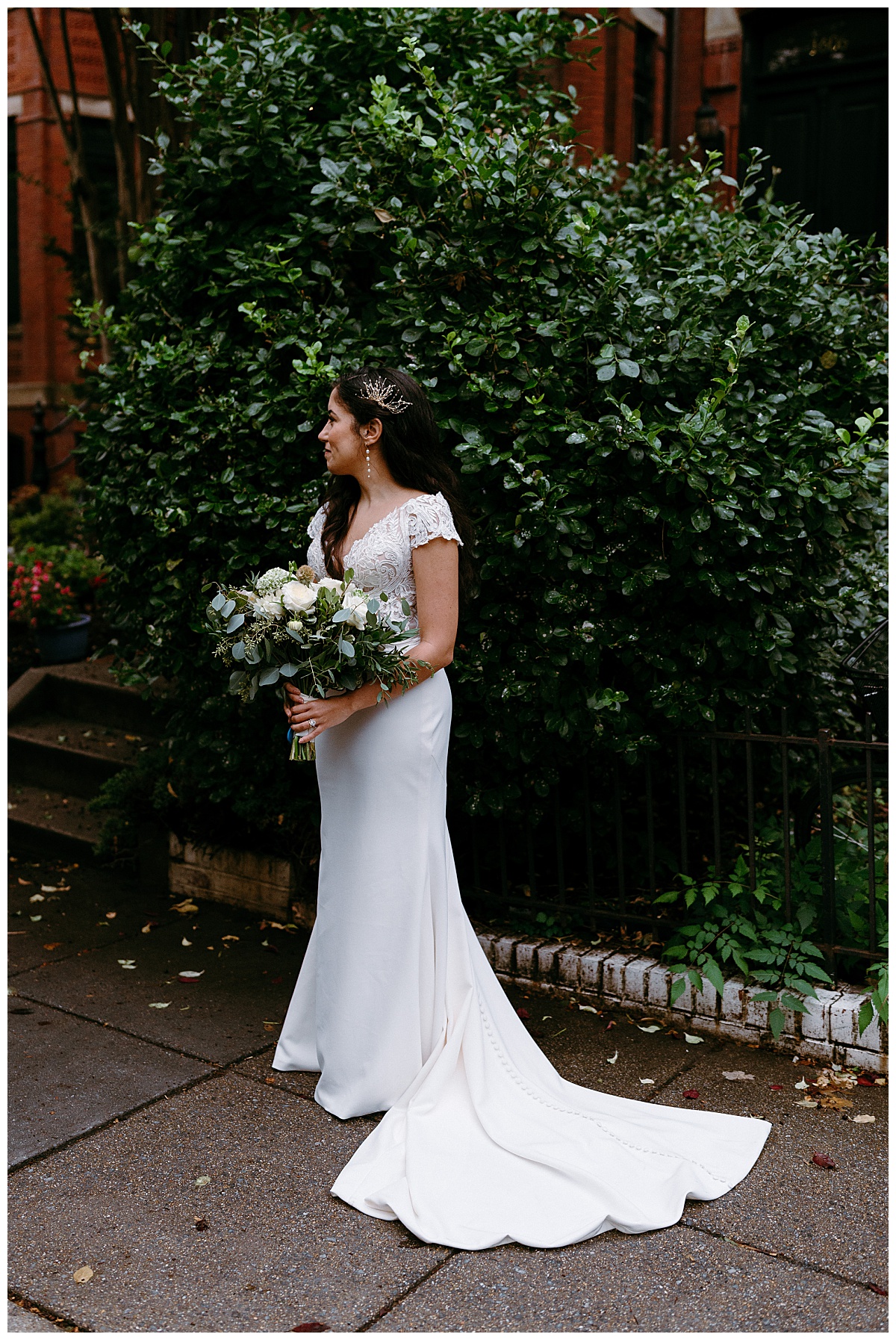 bride holds bouquet and looks to the side in front of greenery by destination wedding photographer