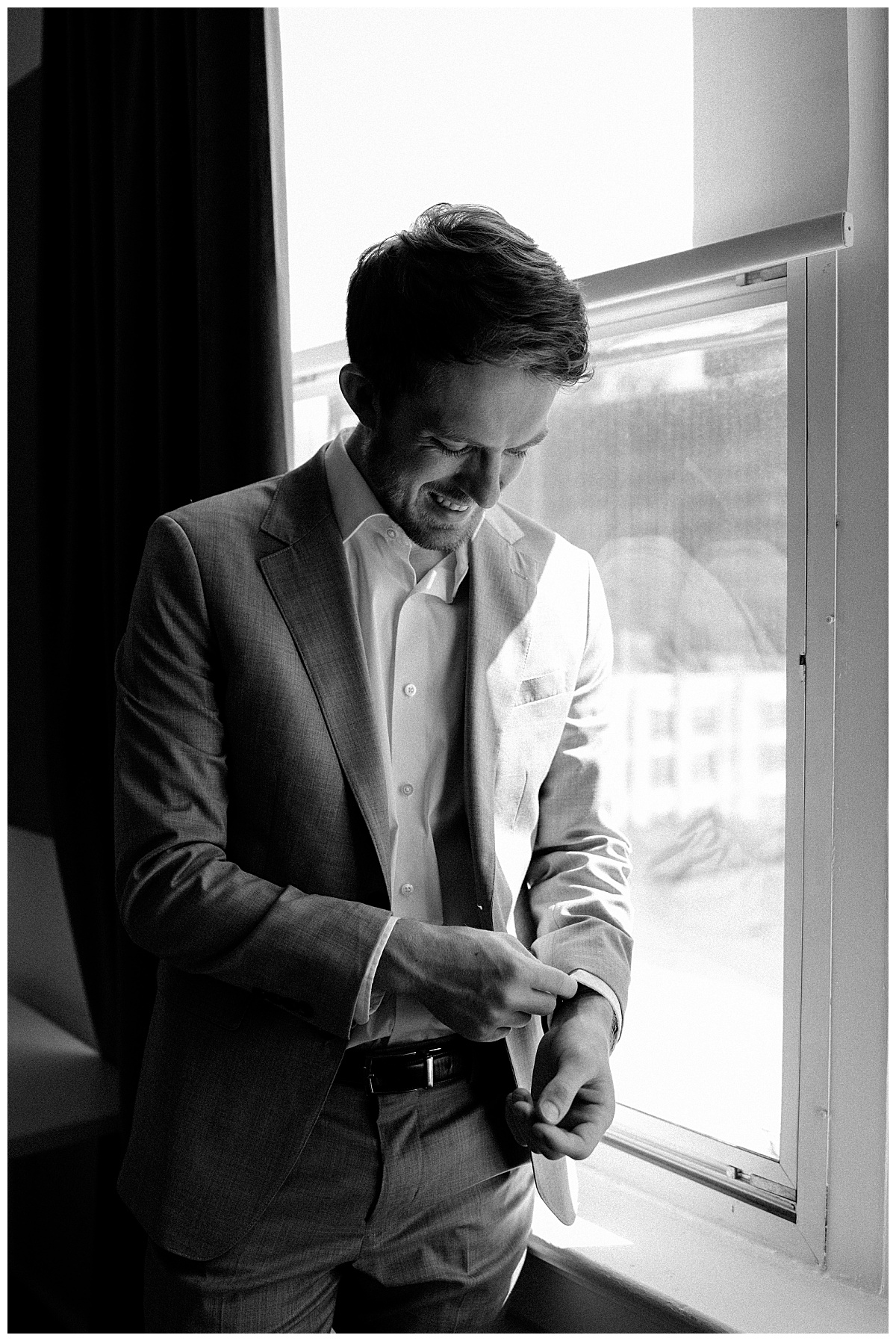 groom adjusts cuffs of shirt in front of window at the Cannon Room