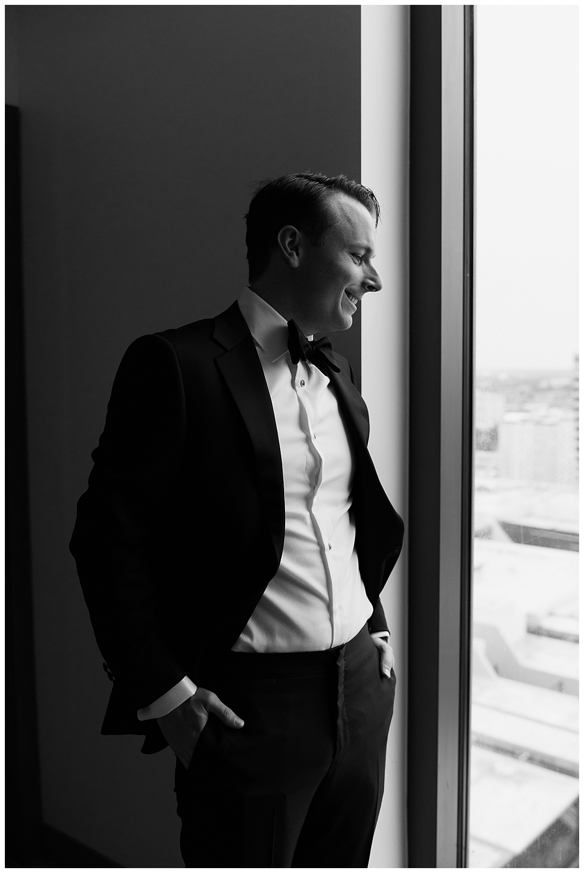 man looks out window with hands in pockets by Charlotte wedding photographer
